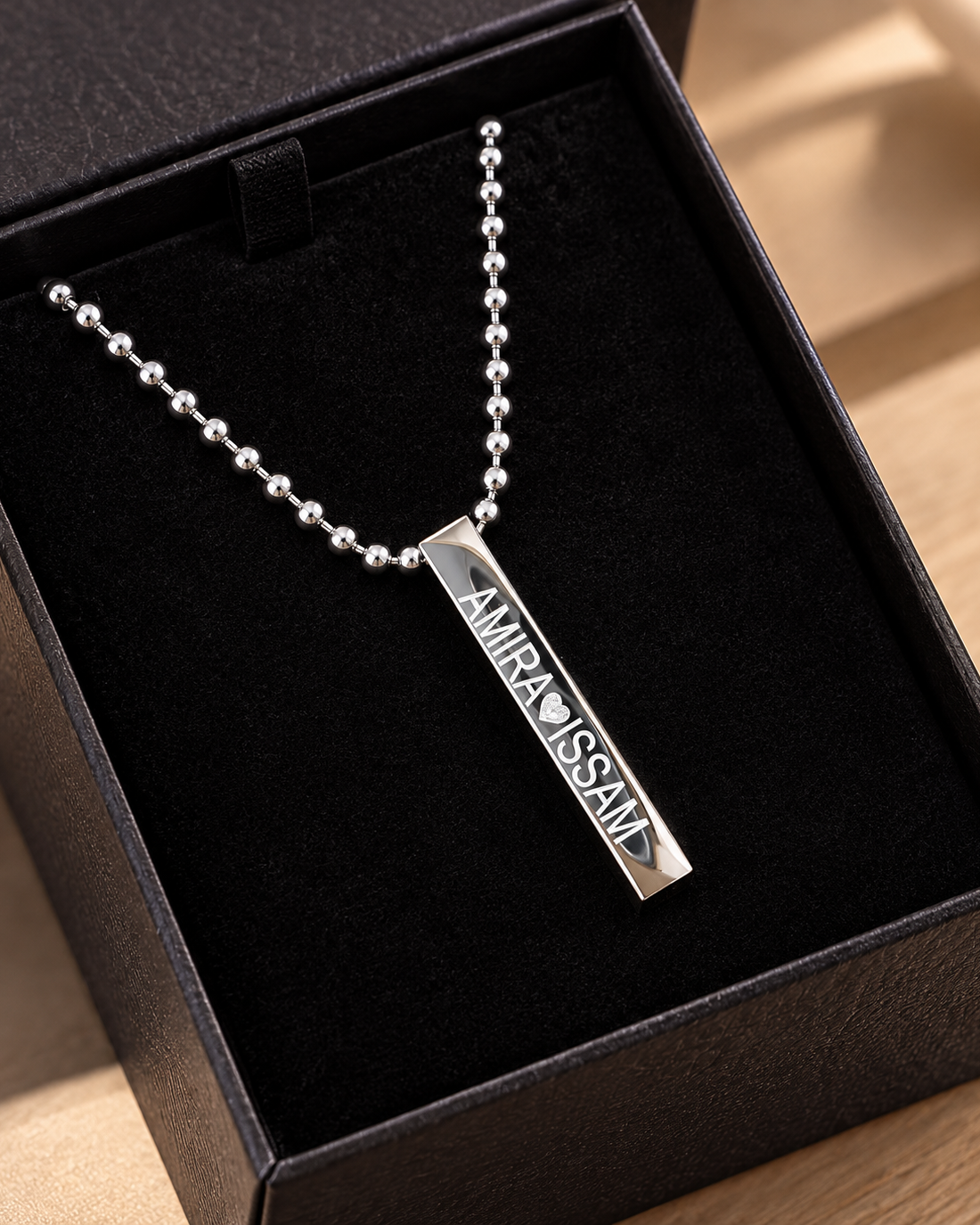 Collier personnalisé homme et femme avec pendentif barre en acier inoxydable gravé Amira et Issam dans son écrin noir.
