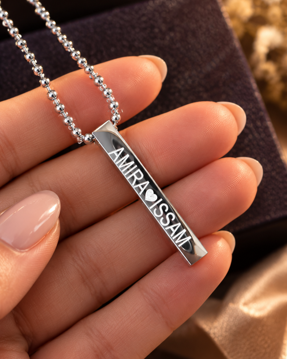 Pendentif barre rectangulaire argenté personnalisé avec gravure prénom et cœur tenu par une main de femme.
