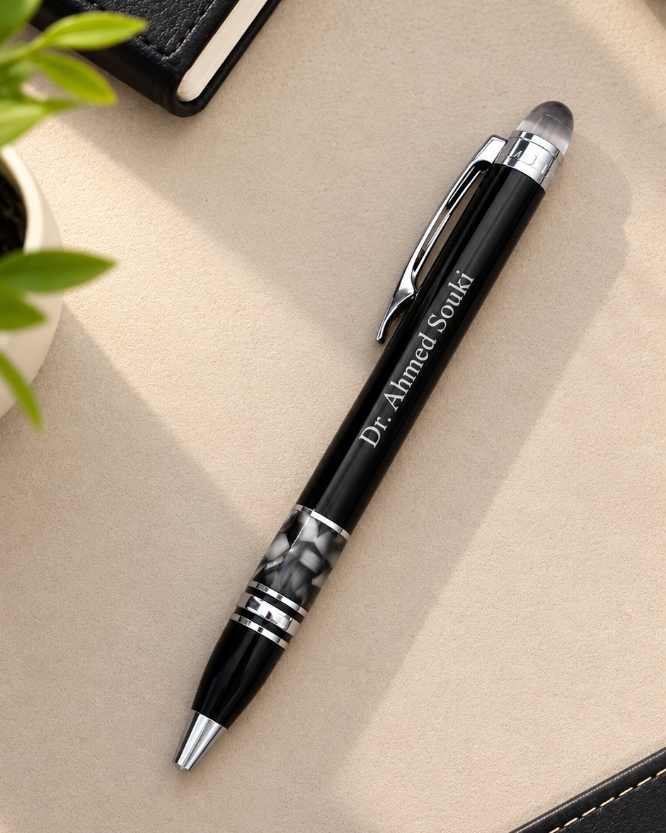 Stylo bille de luxe noir personnalisé avec gravure laser Dr Ahmed Souki posé sur un bureau beige