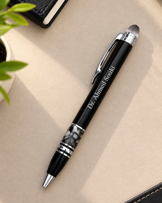 Stylo bille de luxe noir personnalisé avec gravure laser Dr Ahmed Souki posé sur un bureau beige