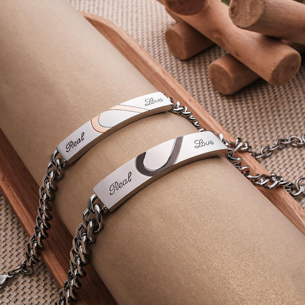 Paire de bracelets gourmettes pour couple en acier inoxydable avec gravure Real Love et motif demi-cœur imbriqué.
